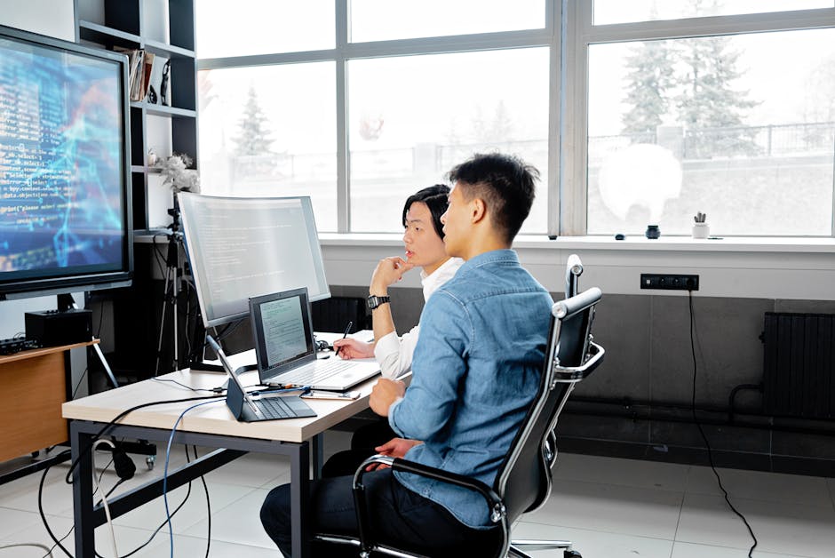 Two men analyzing code on computers in a modern office setting.